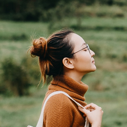 Un portrait de profil d’une femme portant un pull à col roulé ocre et un sac blanc. Elle regarde en l’air et ferme les yeux.